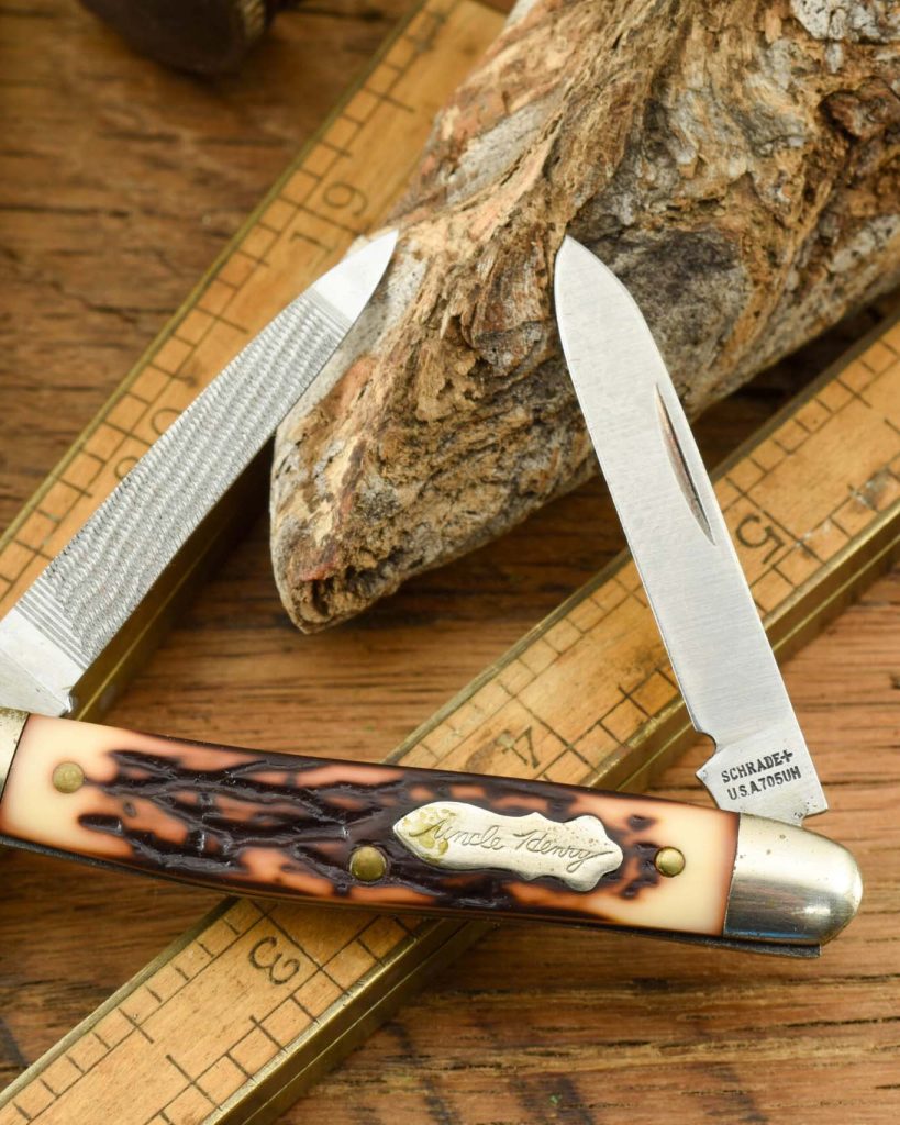 A multi-blade folding knife with a textured bone-like handle inscribed “Uncle Henry” and “SCHRADE+ U.S.A. 705UH,” displayed on a wooden surface with measuring tools and a piece of bark.